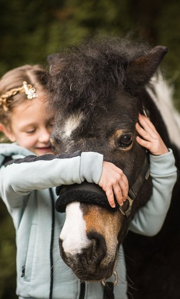 Girl hugging and holding a black pony with a white mark