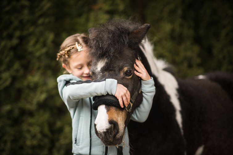 Girl hugging and holding a black pony with a white mark