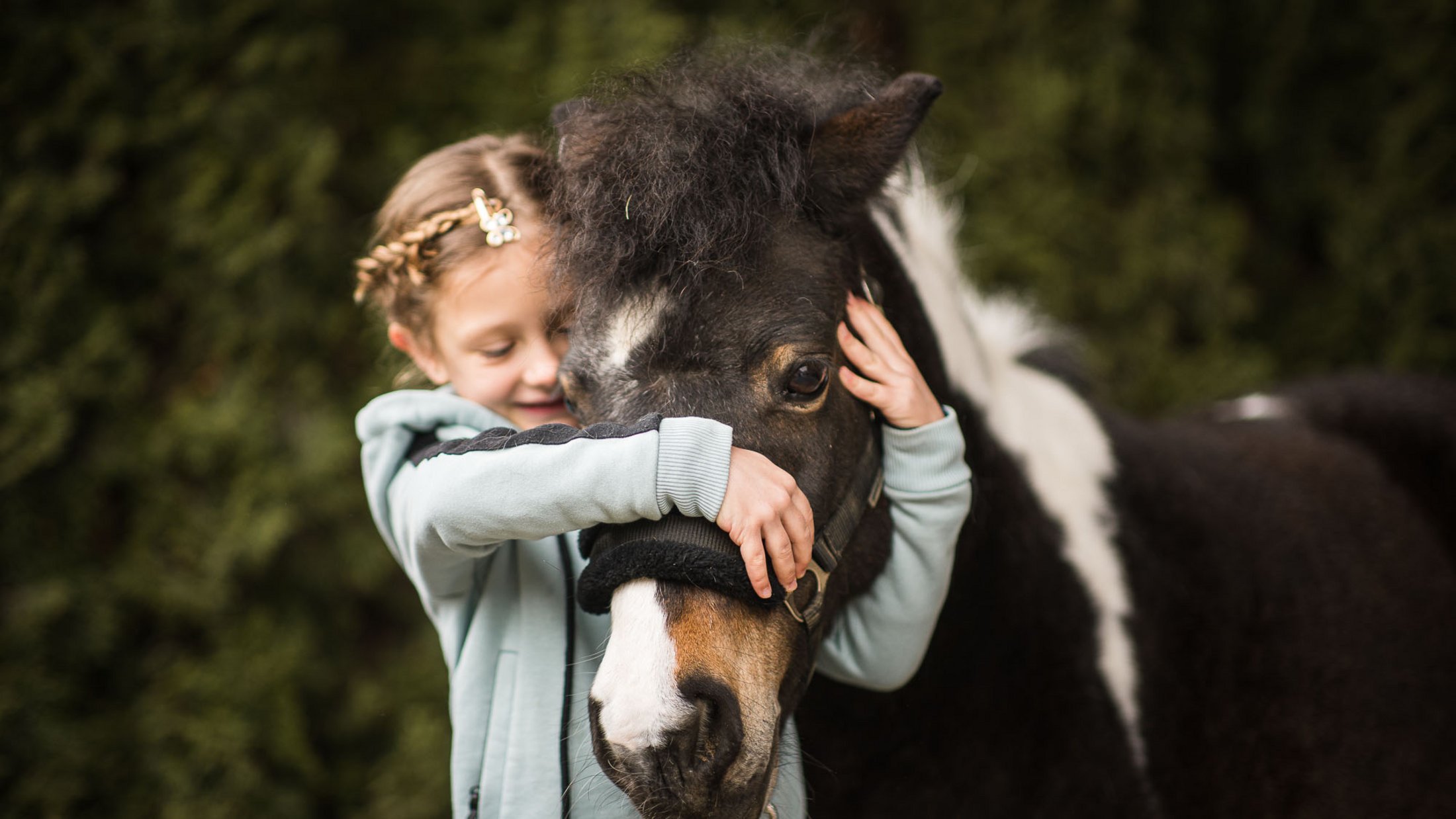 Mädchen umarmt und hält ein schwarzes Pony mit weißem Abzeichen