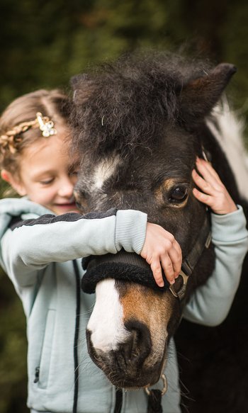 Mädchen umarmt und hält ein schwarzes Pony mit weißem Abzeichen