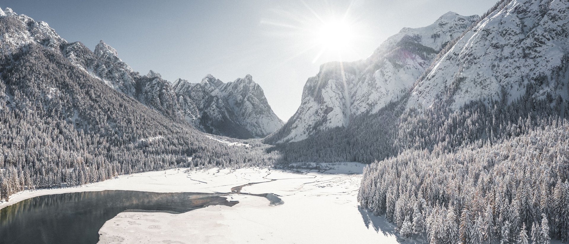 Lago innevato circondato da montagne e foresta sotto il sole