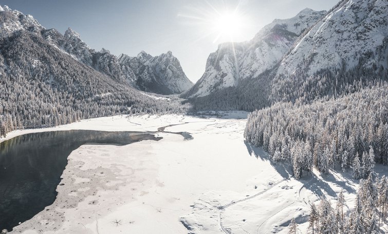 Snow-covered lake surrounded by mountains and forest in sunlight