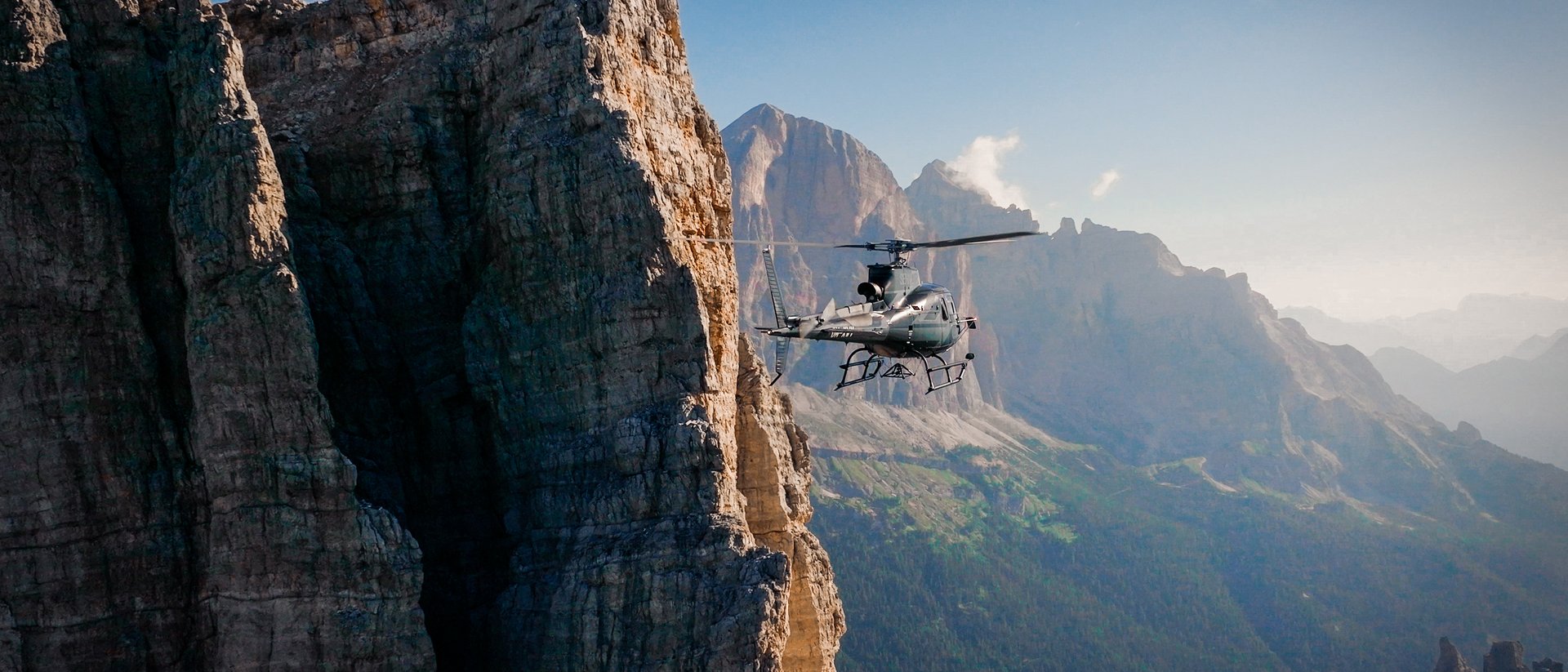 Hubschrauber fliegt neben steiler Felswand in den Bergen bei klarem Himmel