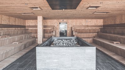 Interno di una grande sauna con panche in legno e forno a pietra al centro