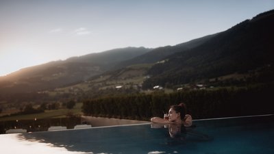 Frau entspannt sich im Pool mit Bergblick bei Sonnenuntergang