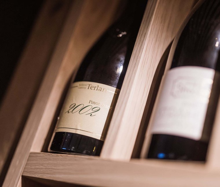 Winkler’s Stories: i nostri alberghi con maneggio di cavalli Bottiglie di vino, tra cui Pinot Bianco 2002, in scaffale di legno