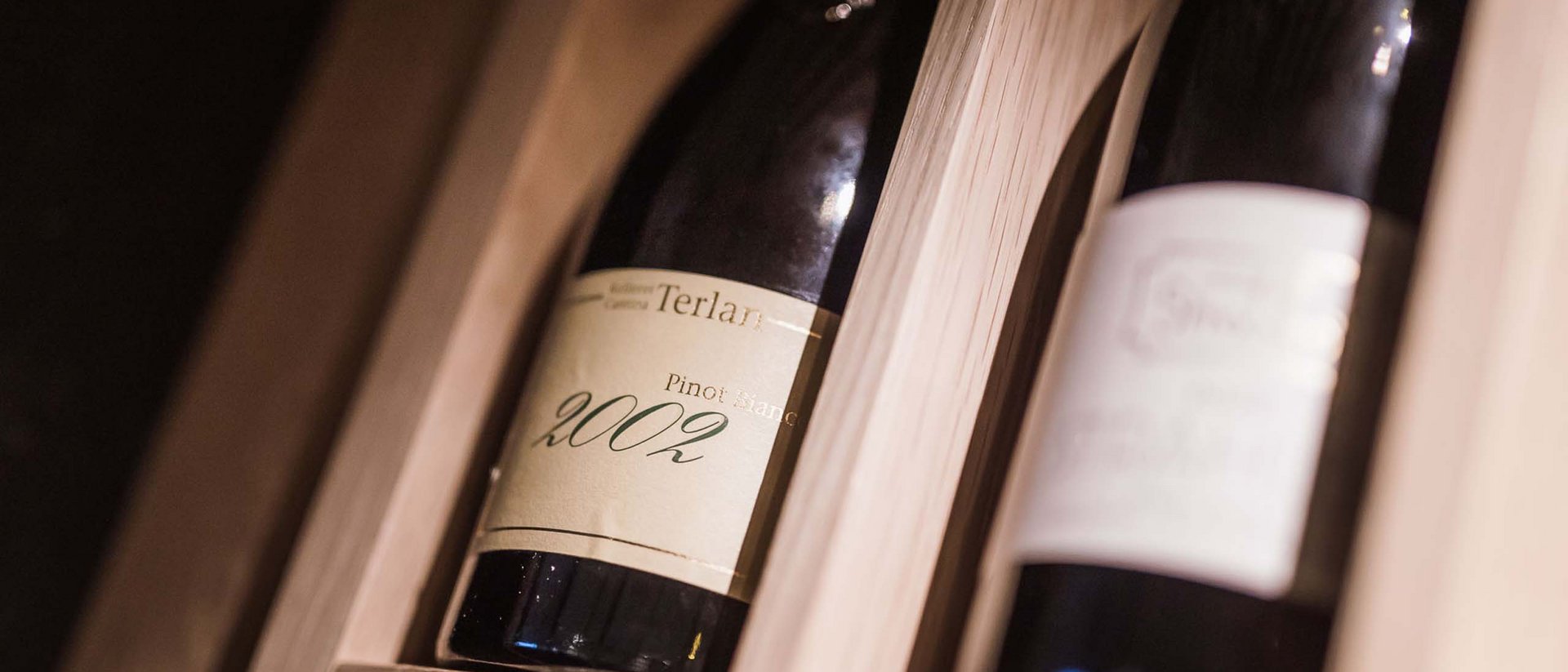 Bottiglie di vino, tra cui Pinot Bianco 2002, in scaffale di legno