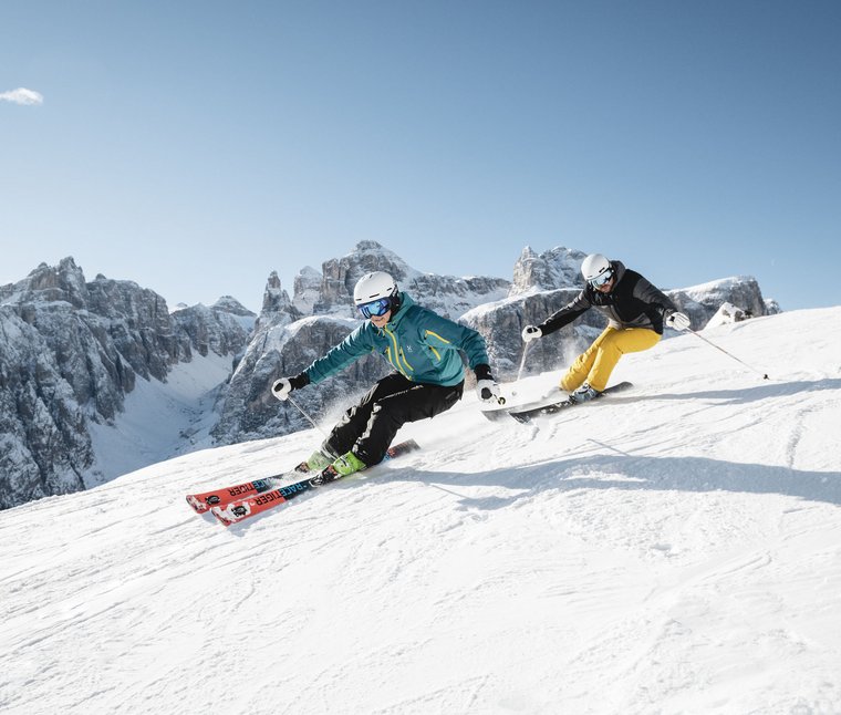 Due sciatori con abbigliamento colorato sciano velocemente su una pista innevata in montagna
