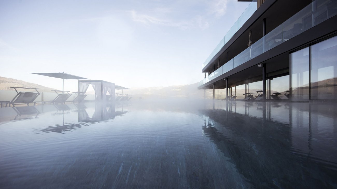Foggy outdoor pool with lounge chairs and modern glass architecture