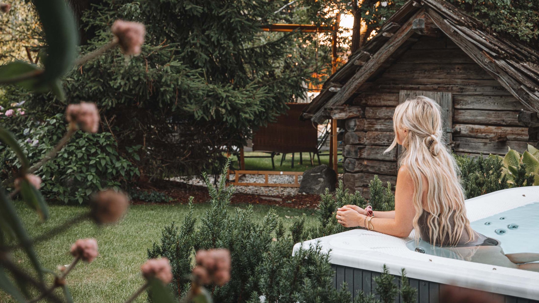 Woman relaxing in garden hot tub beside a small wooden cabin