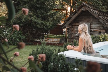 Donna si rilassa nella vasca idromassaggio in giardino vicino a una casetta di legno