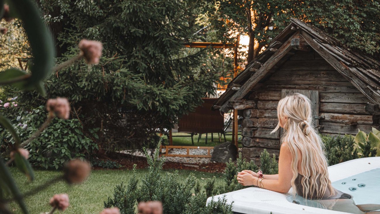 Frau entspannt im Whirlpool im Garten neben einem kleinen Holzhaus