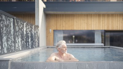 Uomo anziano rilassato in piscina esterna di una casa moderna