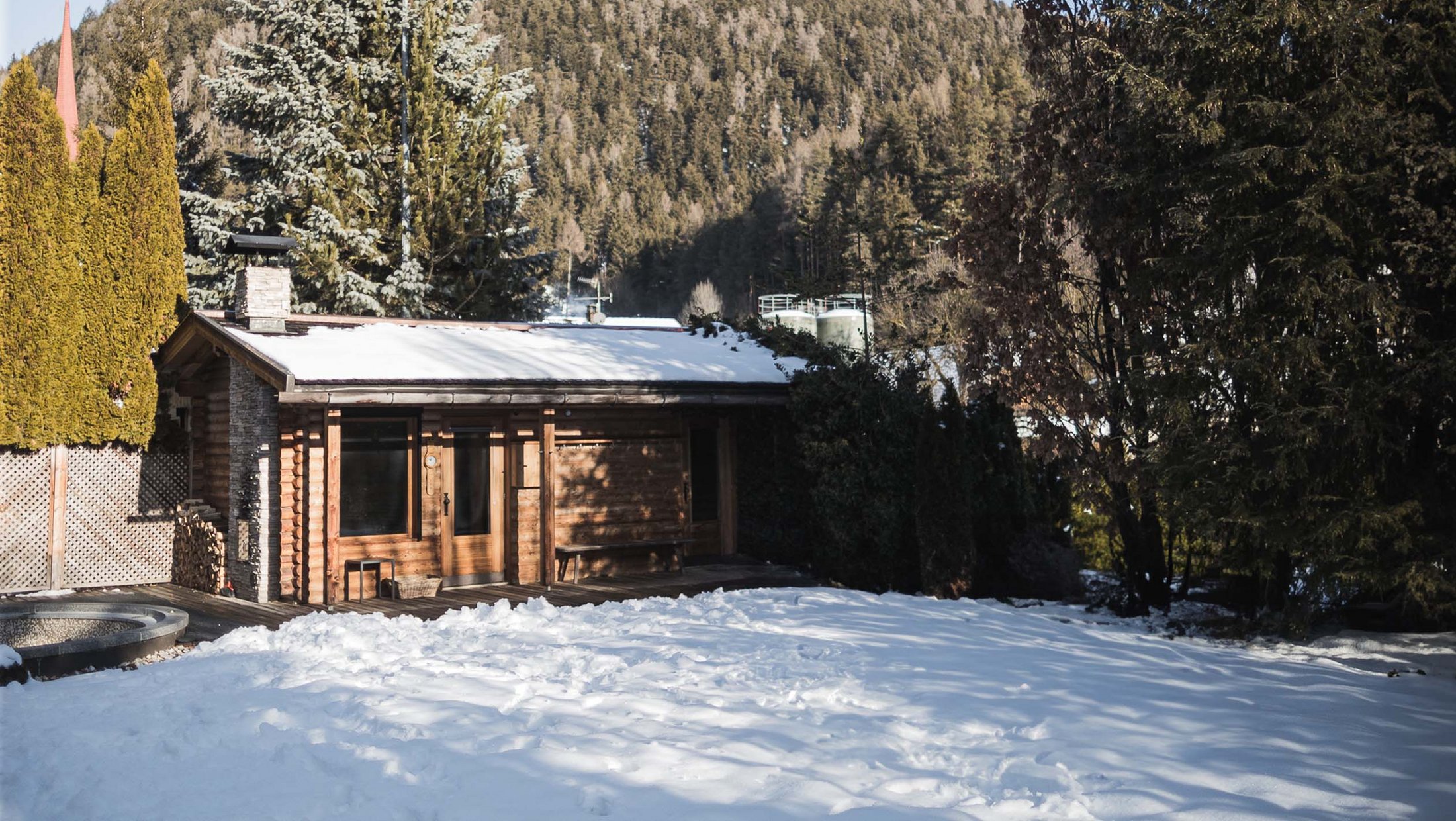 Casa in legno con tetto coperto di neve e giardino davanti a collina boscosa