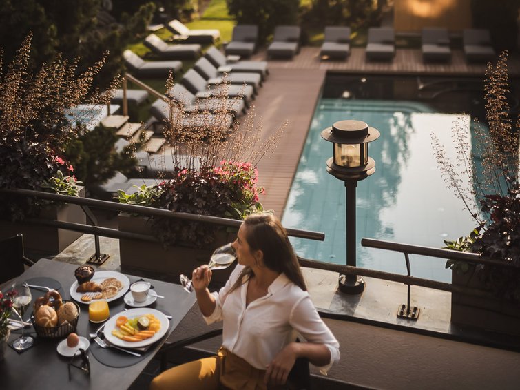 Frau genießt Getränk und Frühstück auf Terrasse mit Blick auf Pool und Garten
