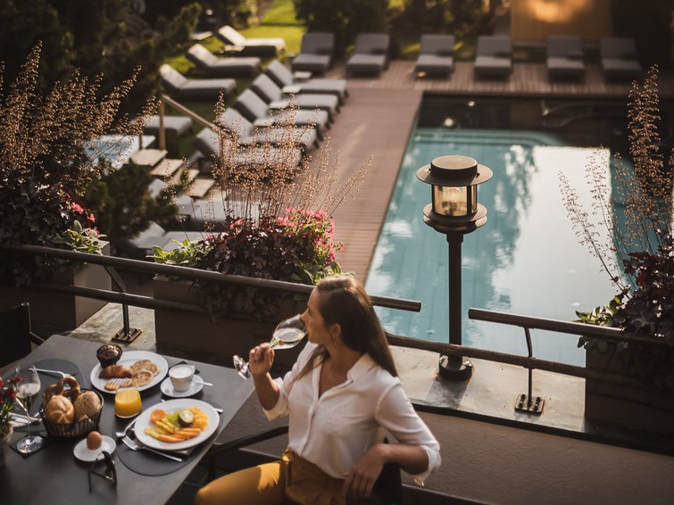 Donna che beve e fa colazione sulla terrazza con vista sulla piscina e sul giardino