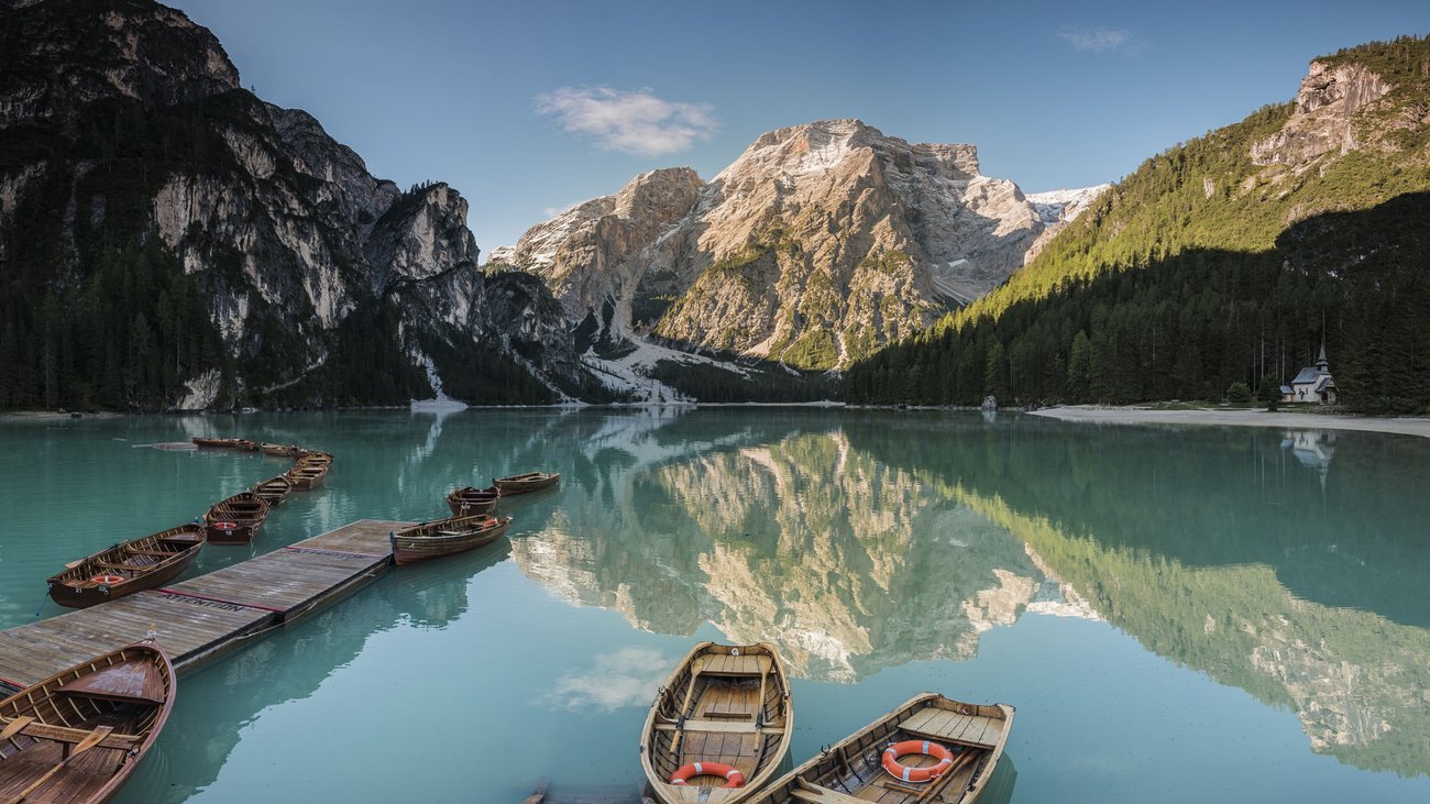 Boote auf klarem Bergsee mit Spiegelung der Berge und Wald im Hintergrund