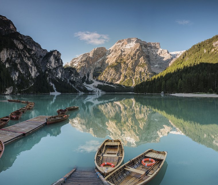 Winkler Stories: Geschichten aus Ihren Hotels im Pustertal Boote auf klarem Bergsee mit Spiegelung der Berge und Wald im Hintergrund