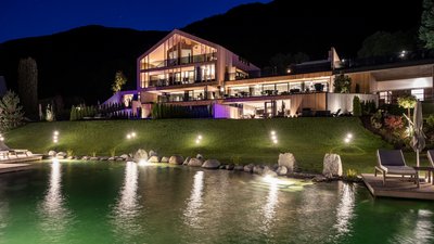L’esclusività in foto: il nostro chalet in Alto Adige di lusso Casa moderna illuminata con giardino e piscina di notte davanti alle montagne