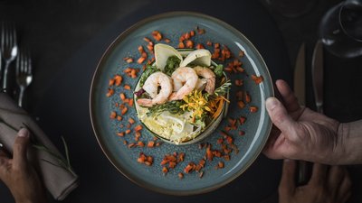 Insalata con gamberi e verdure su piatto blu-verde con pezzi di carota decorativi