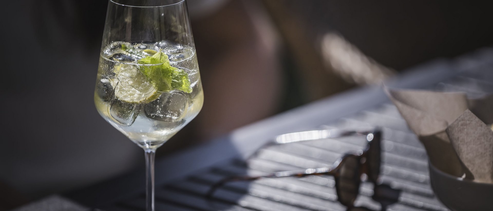 Benedizione delle erbe, Perseidi e divertimento a Ferragosto Bicchiere da vino con ghiaccio, menta e lime su un tavolo con occhiali da sole sullo sfondo