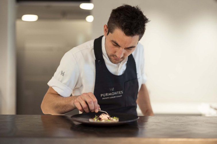 Koch richtet konzentriert ein Gericht auf einem schwarzen Teller an