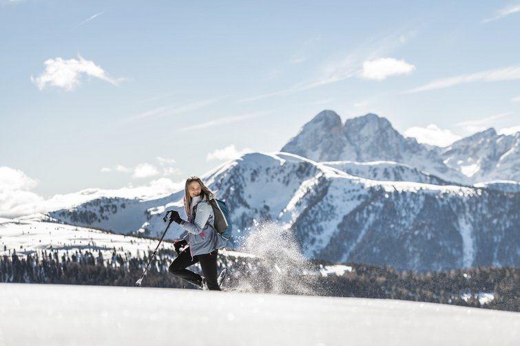 Frau wandert mit Stöcken durch verschneite Berglandschaft bei Sonnenschein