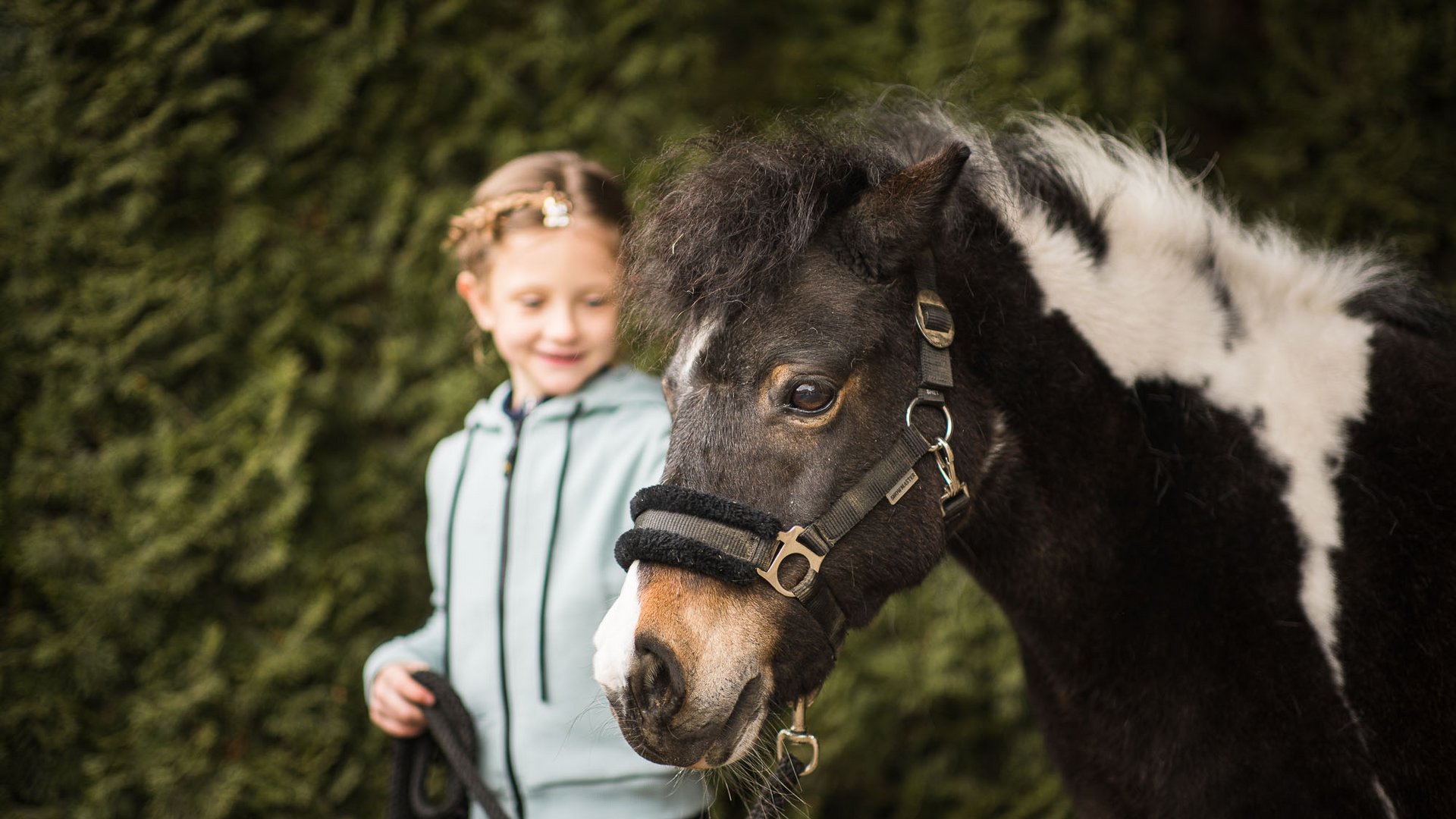 Bambina con giacca azzurra tiene la corda di un pony bianco e nero