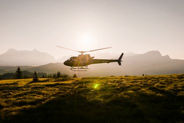 Hubschrauber im Flug über eine sonnige Bergwiese bei Sonnenuntergang