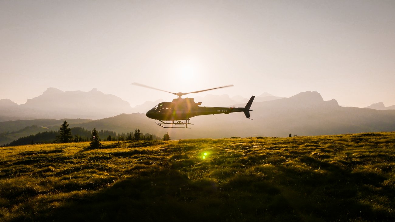 Hubschrauber im Flug über eine sonnige Bergwiese bei Sonnenuntergang
