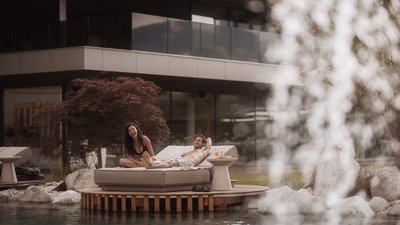 Photos from your hotel in Pfalzen in Val Pusteria/Pustertal Couple relaxing on a lounge chair by a pond and modern house