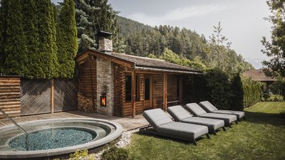 The best photos from our hotel in South Tyrol that kids love Wooden sauna with round hot tub and lounge chairs in garden with mountain backdrop