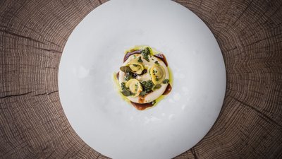 L’esclusività in foto: il nostro chalet in Alto Adige di lusso Ravioli finemente impiattati con salsa su piatto bianco su fondo in legno