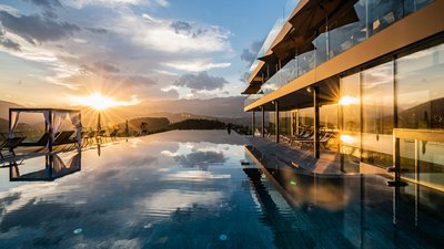 Tramonto su piscina a sfioro con lettini moderni e edificio con vetrate