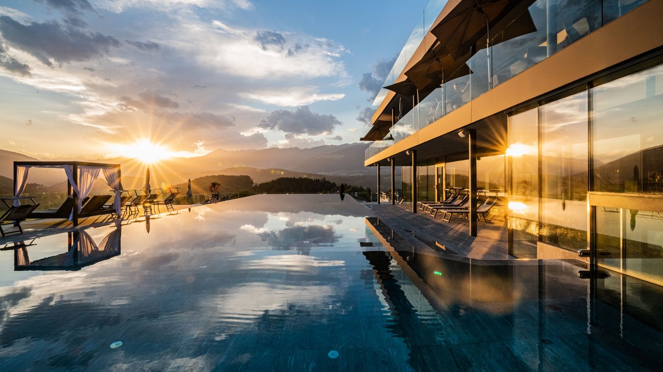 Sunset over infinity pool with modern lounge chairs and glass building