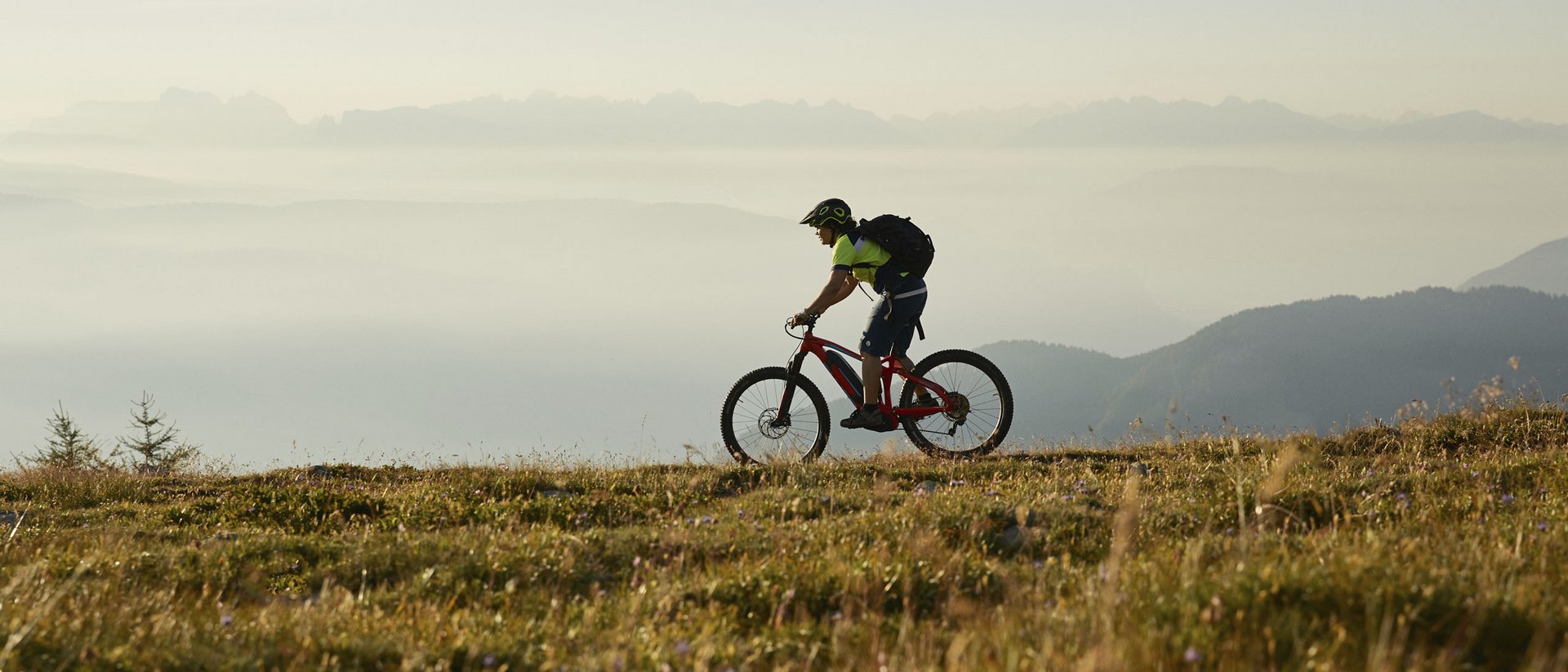 Mountainbiker fährt auf einem Grasweg mit nebelverhangenen Bergen im Hintergrund