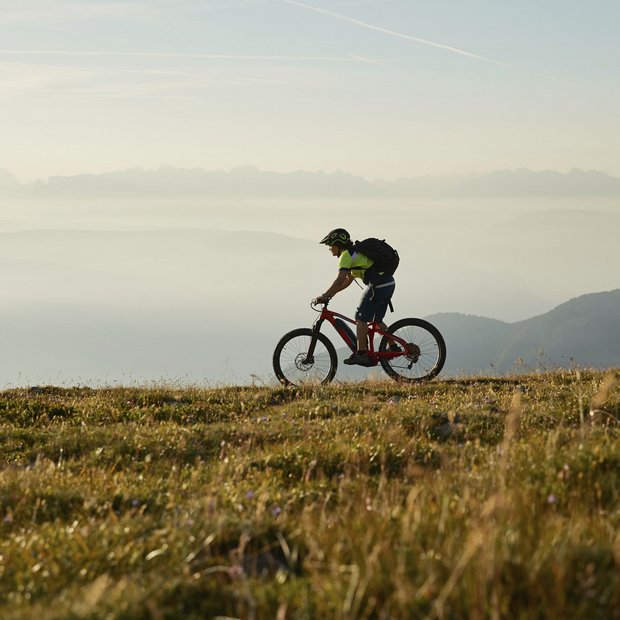 Mountain biker riding on grassy trail with misty mountains in the background