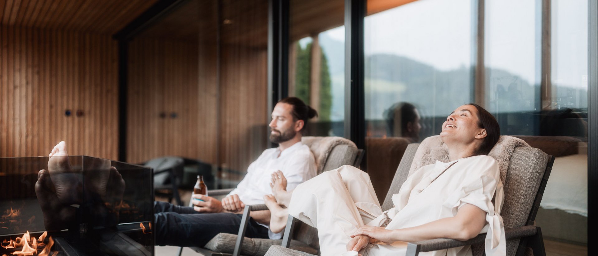Exklusive Suiten in Ihrem Chalet in Südtirol Paar entspannt auf Stühlen neben einem Kamin in modernem Haus