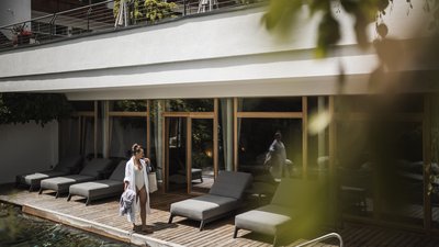 The best photos from our hotel in South Tyrol that kids love Woman in swimsuit and robe by pool with lounge chairs and wooden deck