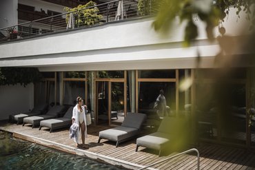 Donna in costume da bagno e accappatoio vicino alla piscina con lettini e pavimento in legno