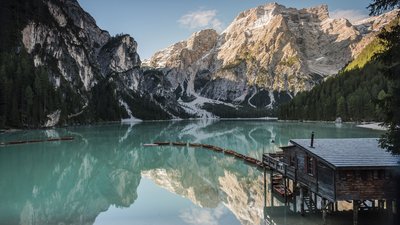 Lago di montagna tranquillo con barche di legno davanti a una casa sul lago e montagne innevate