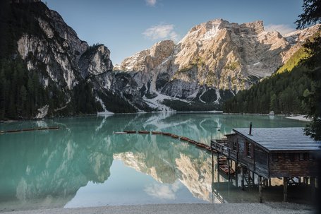 Calm mountain lake with wooden boats by a boathouse and snow-capped mountains