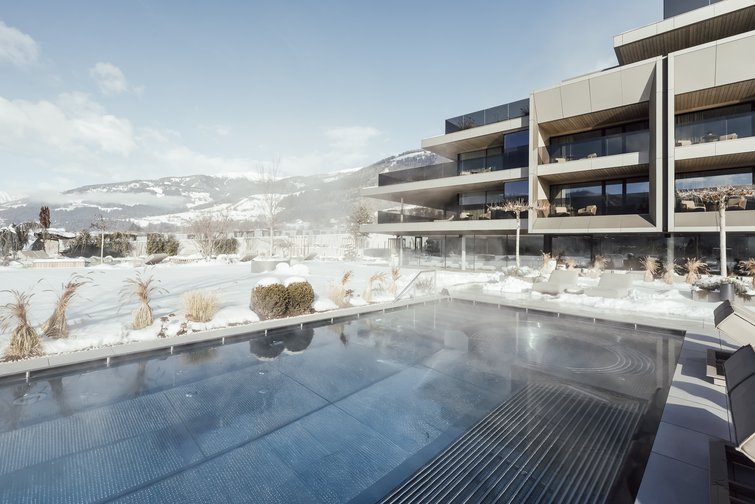 The multi-faceted Sonnenspa at our spa hotel in South Tyrol Heated outdoor pool with snow and modern building in the background