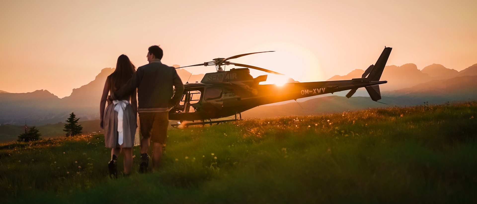 Coppia cammina al tramonto verso un elicottero in un prato di montagna