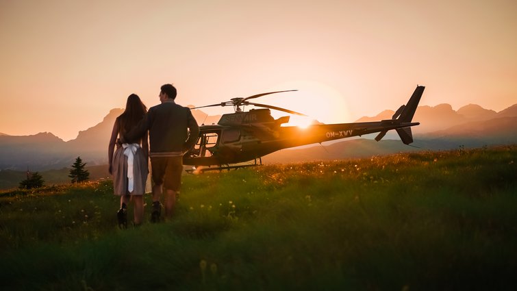 Coppia cammina al tramonto verso un elicottero in un prato di montagna
