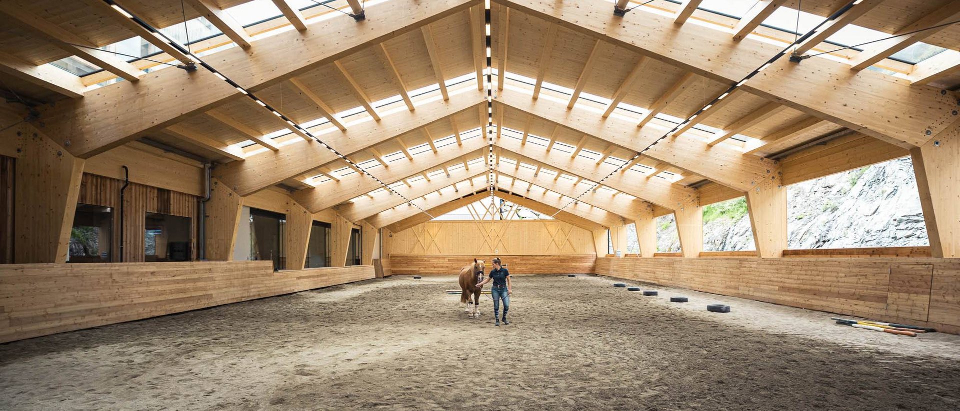 Mann führt Pferd in einer modernen Reithalle aus Holz