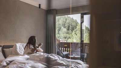 The best photos from our hotel in South Tyrol that kids love Woman sitting in bed looking at balcony with forest view