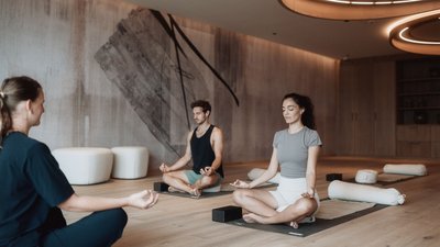 Photos from your hotel in Pfalzen in Val Pusteria/Pustertal Three people meditating on yoga mats in a modern yoga studio