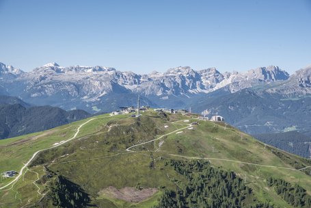 Green hill with paths and buildings in front of snow-capped Alpine peaks