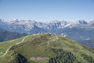 Grüner Berg mit Wegen und Gebäuden vor schneebedeckten Gipfeln der Alpen